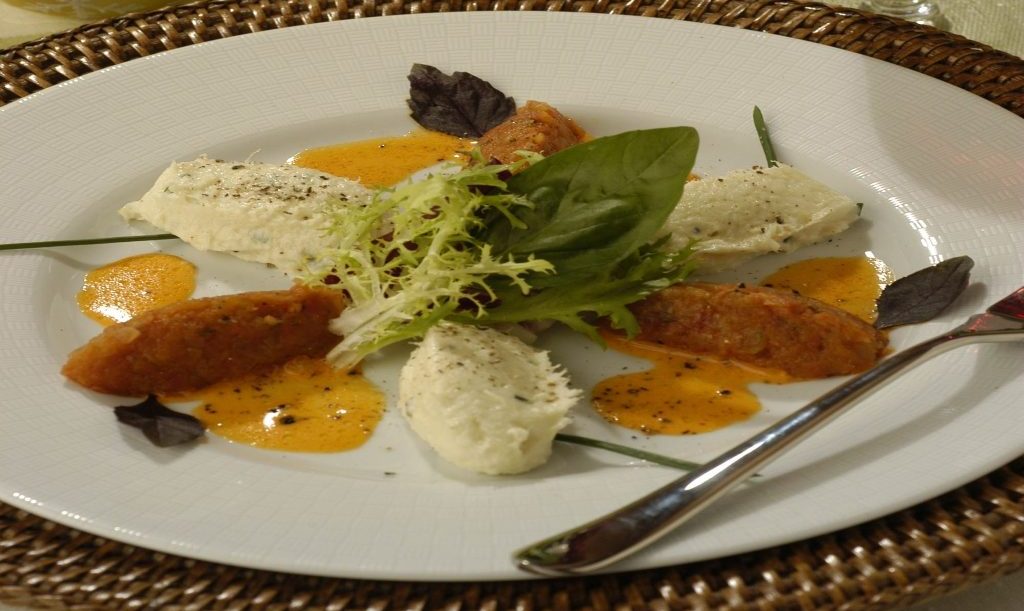 Foto de bacalhau em pasta com coulis de pimentão servidos com folhas no prato.
