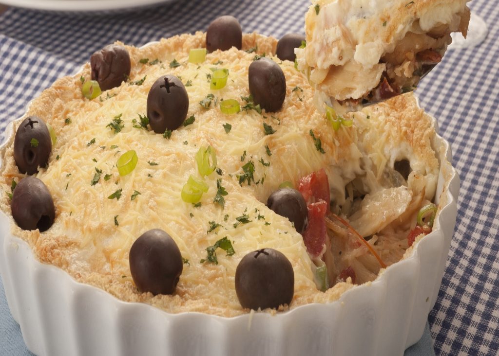 Foto de bacalhau divino na travessa com azeitonas por cima. Um pedaço é retirado e destacado na imagem.