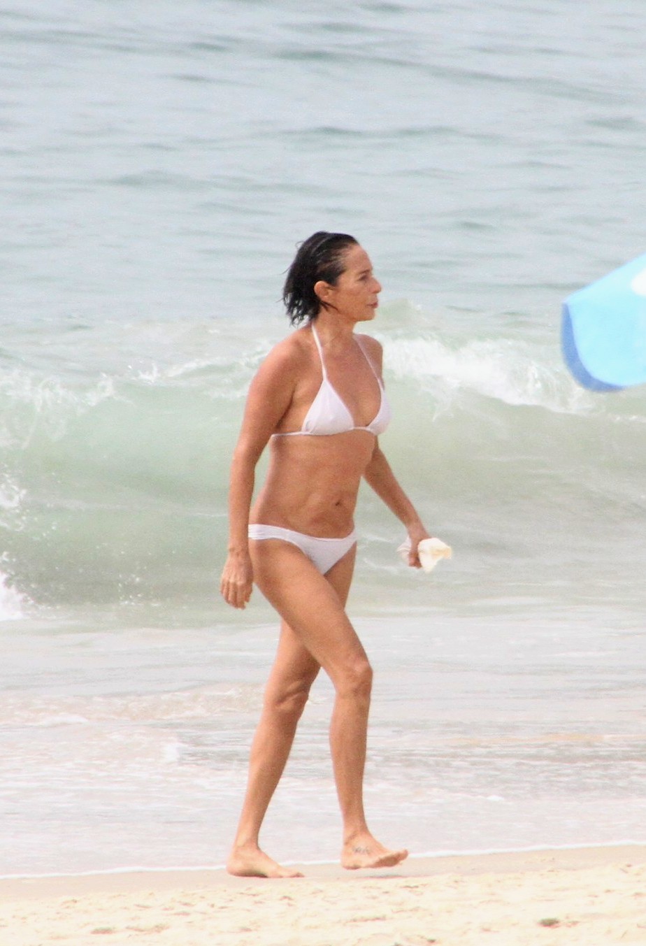 Mulher branca, de cabelo curto, usando um biquíni branco e saindo do mar segurando um pacote branco