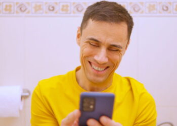 Homem usando celular no banheiro - Créditos: depositphotos.com / ivanmoreno