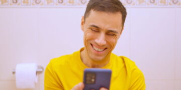 Homem usando celular no banheiro - Créditos: depositphotos.com / ivanmoreno