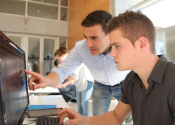 Aluno e professor usando computador - Créditos: depositphotos.com / Goodluz