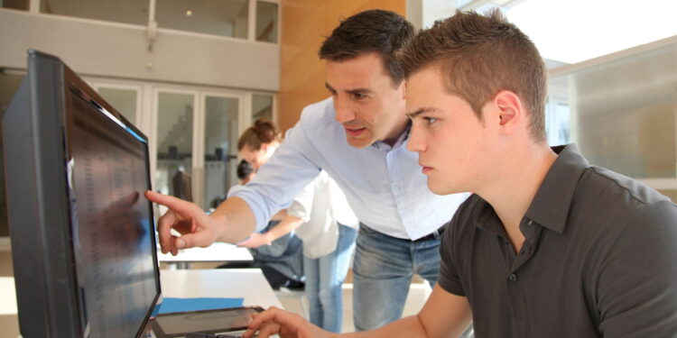 Aluno e professor usando computador - Créditos: depositphotos.com / Goodluz