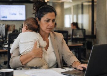 Mulher no escritório com bebê no colo enquanto trabalha, ilustrando o impacto da maternidade na carreira feminina