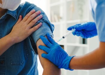 Young Asia lady nurse giving Covid-19 or flu antivirus vaccine shot to senior male patient wear face mask protection from virus disease at health clinic or hospital office. Vaccination concept.